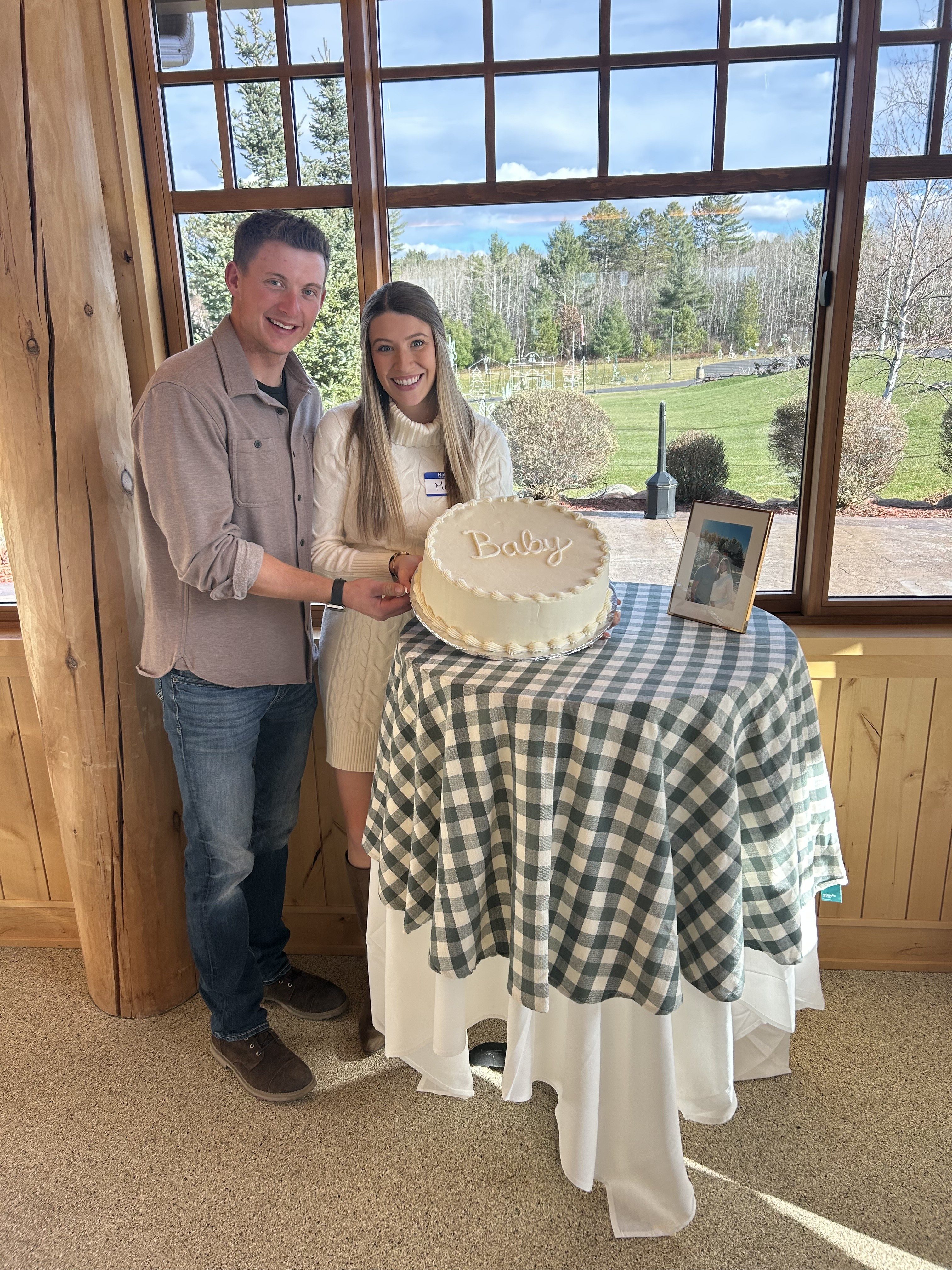 A couple with cake standing in front of window during their baby shower